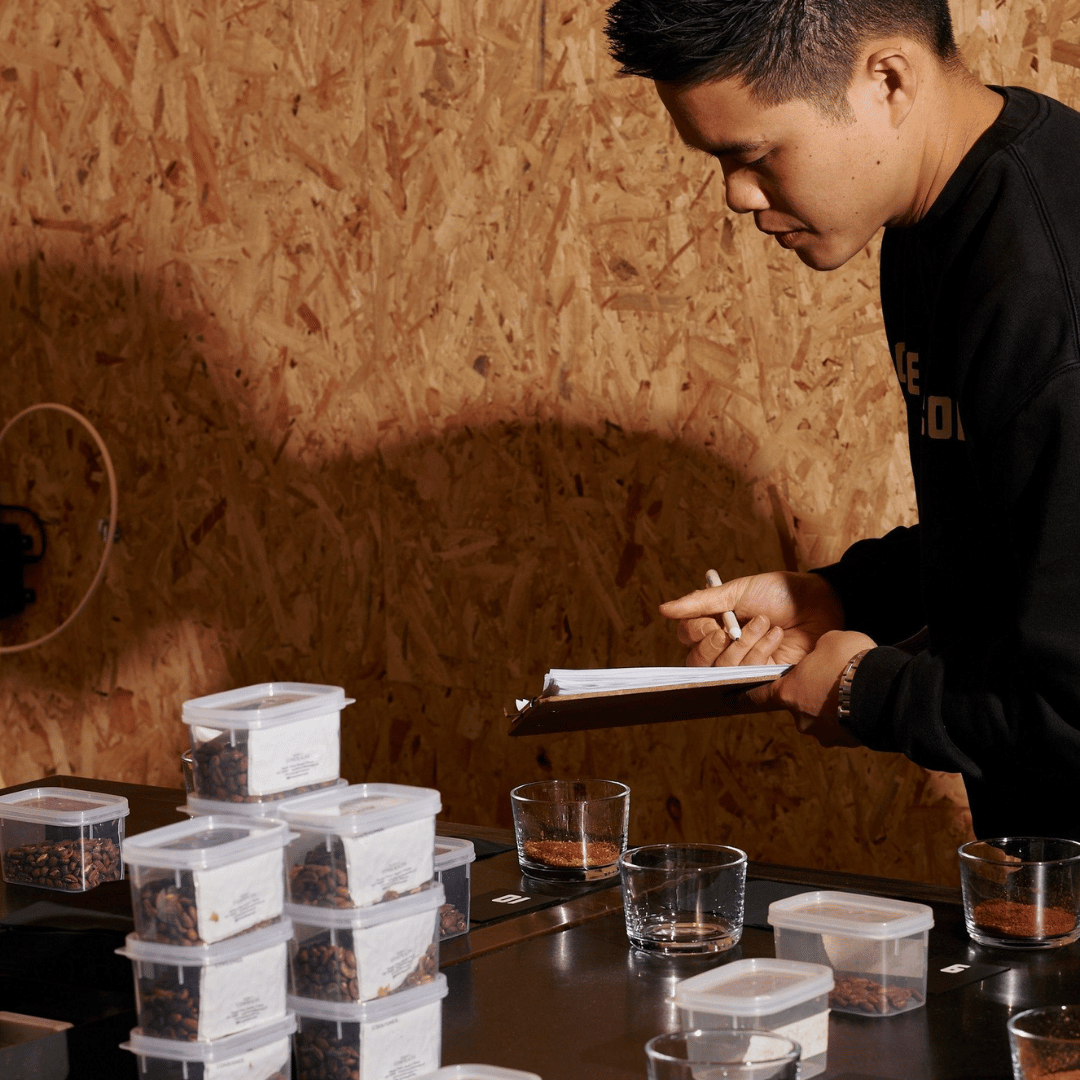 Person taking notes at a table with containers and glasses against a wooden wall.