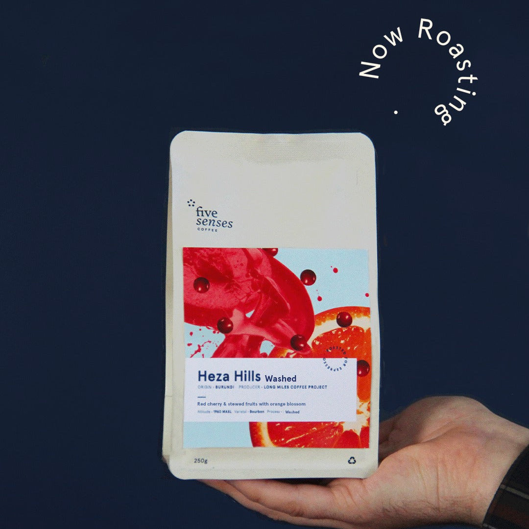 Hand holding a coffee package labeled 'Heza Hills Washed' against a dark background