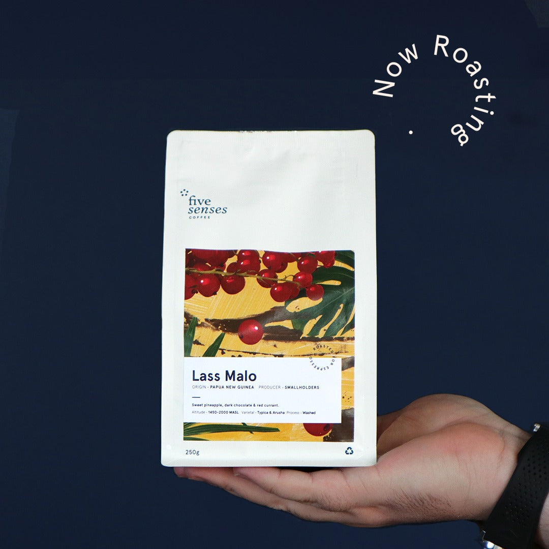 Hand holding a coffee package labeled 'Lass Maio' with a dark blue background