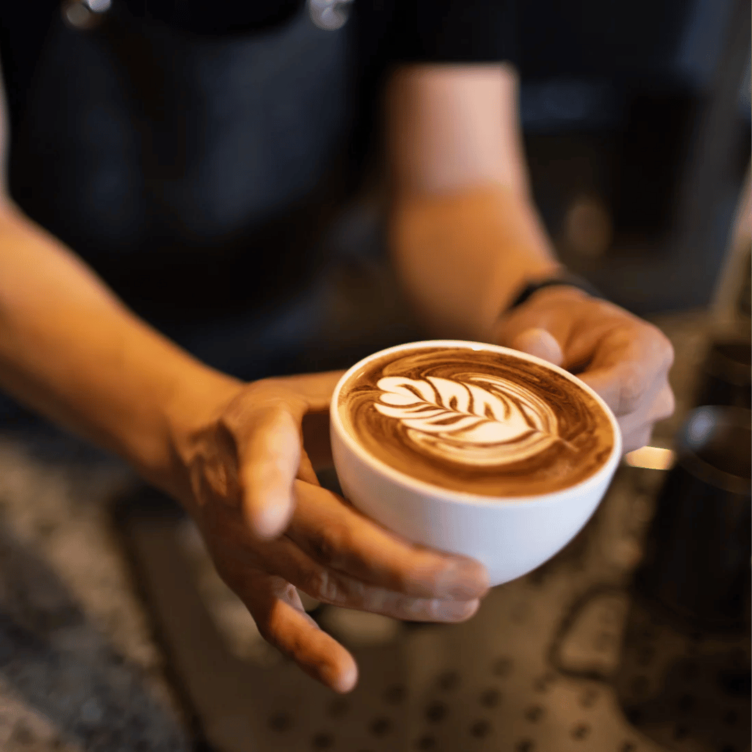 Person holding a cup of coffee with latte art in a bar setting