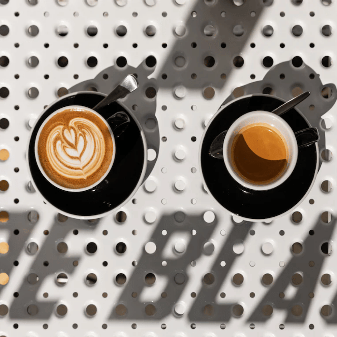Two coffee cups with different types of coffee on a pegboard background with 'BLOOM' branding.